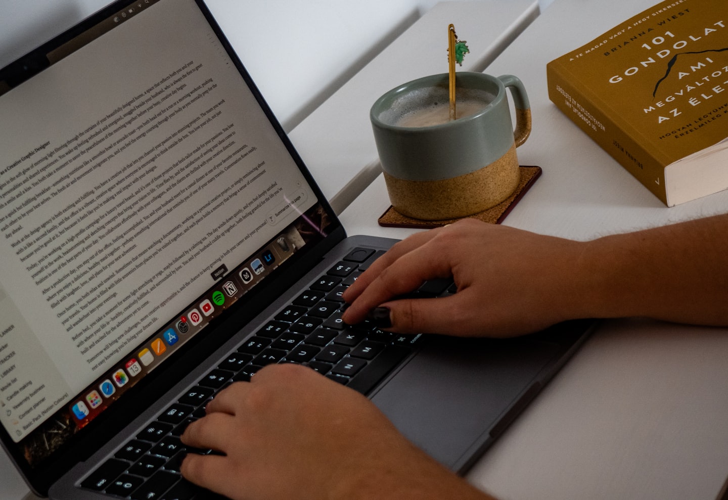 Hände tippen auf einem Laptop neben einer Tasse und einem Buch.